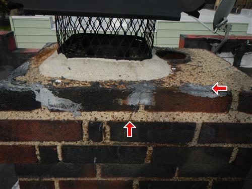 Brick chimney top with a cement cap, mesh rain cap and red arrows at cracks in the cap and the seal to the brick.