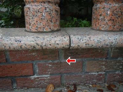 Granite coping on a brick wall under two polished stone columns, red arrow at an open joint in the coping.