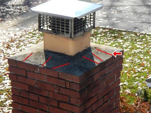 A brick chimney with a screened cap, its cracked concrete crown marked with red lines.