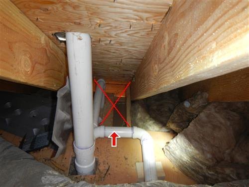 PVC drain piping in a crawlspace with an improper fitting marked with a red X.