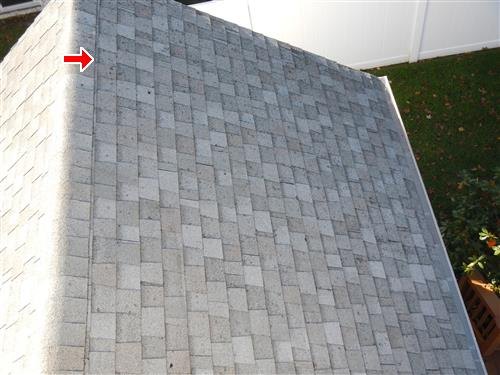 Gray asphalt shingle roof slope viewed from above, red arrow near the ridge