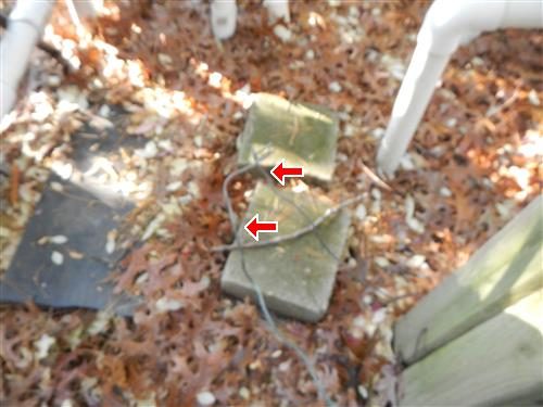 Bare copper grounding wires running across concrete blocks beside white PVC pool piping, marked with red arrows.