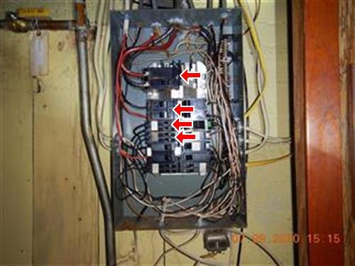 An open electrical panel in a wood-panelled basement with multiple findings marked by red arrows.