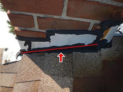 Brick chimney base with black roof cement smeared over flashing, red line and arrow