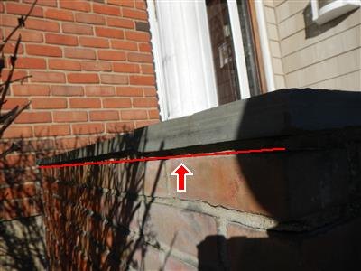 Dark stone cap on an exterior brick wall below a window, red line and arrow at the joint