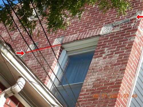 Red brick wall around an upper window with a red line along the lintel and two red arrows pointing at displaced bricks.