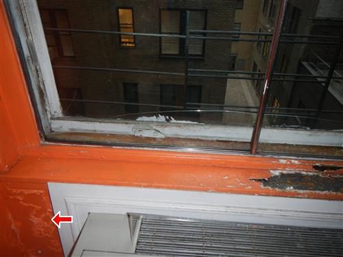 Orange painted window surround with peeling paint and damaged wall below the sill, marked by a red arrow.