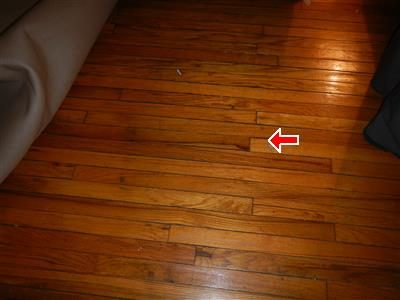Hardwood floor boards with a visible gap between two boards, marked by a red arrow.