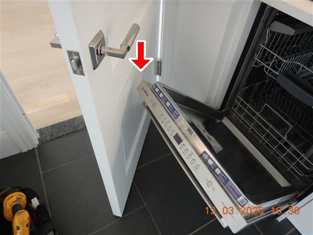 White kitchen door swung open against the lowered door of a dishwasher, with a red arrow at the contact point.