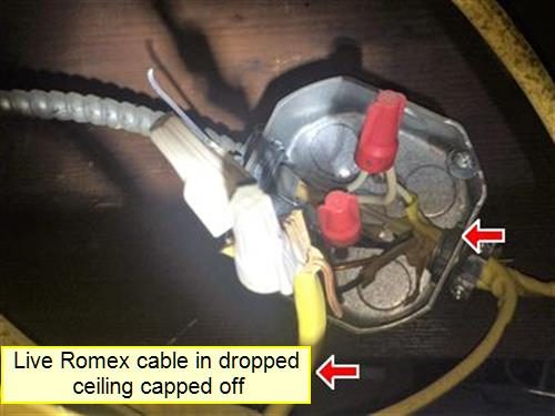 Open metal junction box in a dark ceiling with wire nuts and loose cables, a red arrow and a label about a live Romex cable capped off.