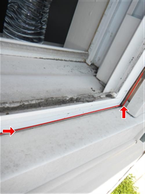 Exterior corner of a white window frame and sill with gaps traced by red lines and two red arrows.