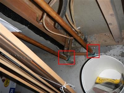 Copper heating pipes under floor joists with two elbow joints outlined in red boxes showing green corrosion.