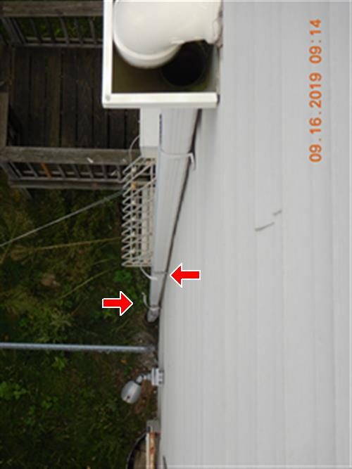 Downward view of a white leader pipe on vinyl siding with two red arrows pointing at the pipe band clamps.