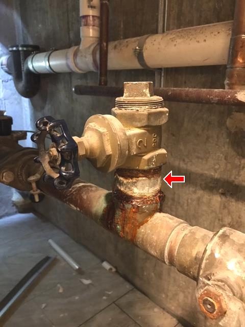 Brass 2-inch water valve on the main service pipe with a heavily rusted steel nipple beneath it, marked by a red arrow.
