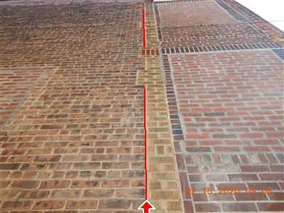 Looking up a brick column where a vertical crack is traced with a red line and a red arrow at the bottom.
