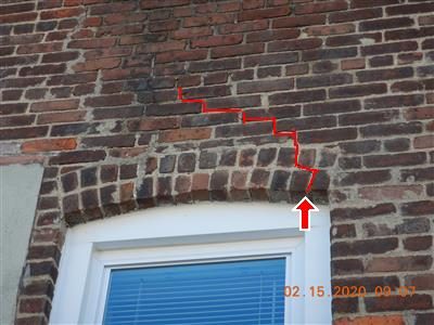 Brick wall above a window arch with a stepped crack traced in red and a red arrow at the arch.