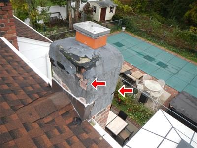 Brick chimney on a shingle roof with peeling black flashing cement on its face, marked by two red arrows.