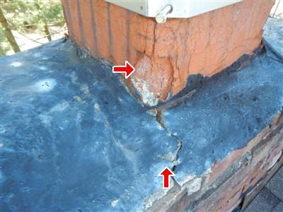 Top of a chimney with a cracked cement cap and crumbling orange clay flue liner, marked by two red arrows.
