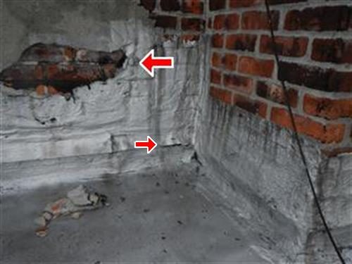 Corner of a brick parapet wall where the silver coating has peeled away exposing brick, two red arrows at the peeled areas.
