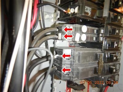 Close view of panel breakers with four red arrows pointing at grey conductors on their terminals.