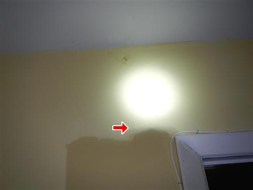 Yellow painted wall above a doorway frame with a red arrow pointing at a hairline crack in the sheetrock.