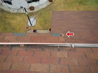 Rear roof overhang with brown shingles beside a gutter, red arrow at a broken shingle corner; pool and patio below.