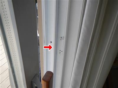 Close-up of a white sliding door frame with empty screw holes where a latch was, marked by a red arrow.