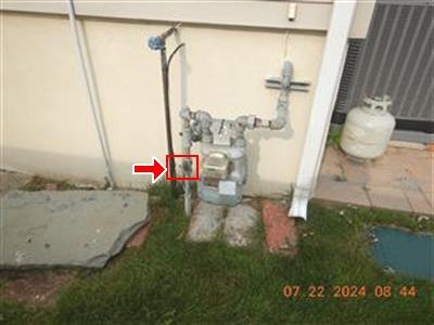 Exterior gas meter and piping against a stucco wall, red box and arrow on a fitting