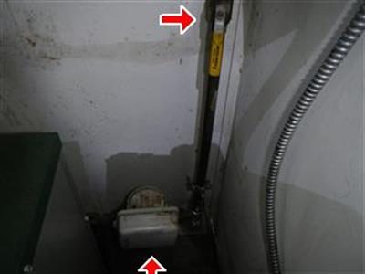 Water meter and shut-off valve on a riser pipe in a boiler room corner, two red arrows marking them.