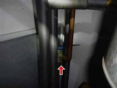Grey pipes beside a boiler with a small valve and blue handle marked by a red arrow.