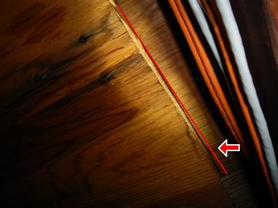 Attic plywood roof sheathing with a long split beside the rafter line, marked by a red line and arrow.