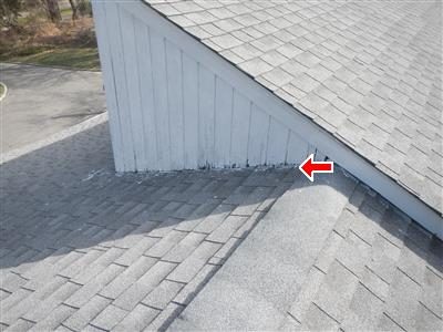 Side of a white dormer where it meets the shingle roof, with dark staining on the lower siding boards, marked by a red arrow.