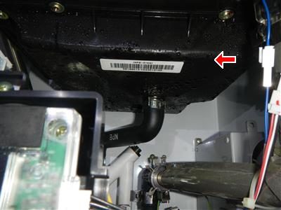 Underside of a black heating unit cabinet with wet condensate residue around a drain fitting, marked by a red arrow.