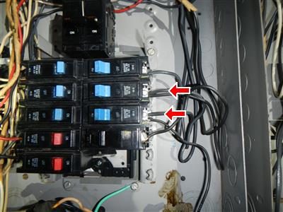 Breakers in a main electrical panel with two red arrows pointing to terminals holding two wires each.