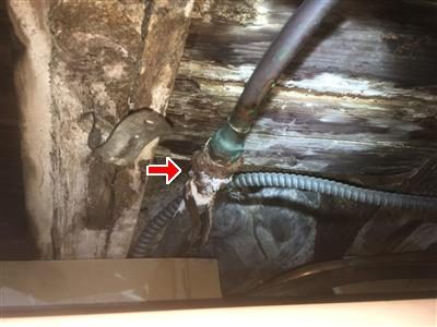 Copper water pipe joined to an older galvanized pipe at a basement ceiling, red arrow at the corroded joint.
