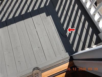 Grey painted balcony deck boards with a red arrow at a split board near the railing.