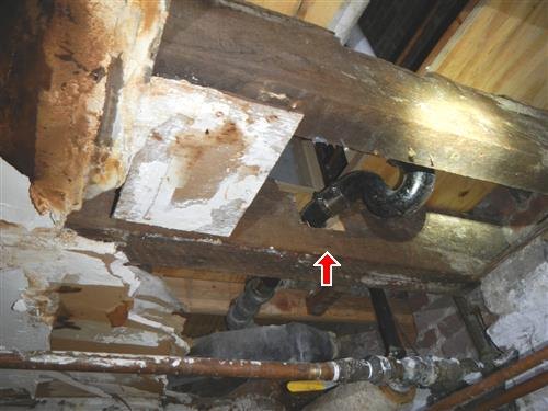 Old wood cellar joists with historic notches, patches and plumbing penetrations, one point arrowed.