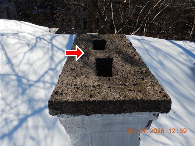 A masonry chimney crown with two open square flues, photographed in winter light, one arrow marking the crown.