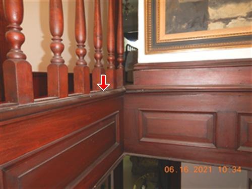 Dark wood stair balustrade and raised paneling with a red arrow at the top rail