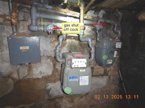 Two gas meters on a stone cellar wall, yellow label and arrows marking the gas shut off cock