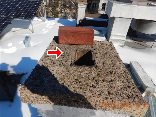 Rooftop chimney cap with an open flue hole and a loose brick on top, red arrow, snow around