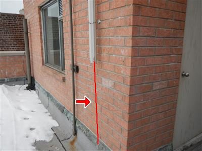 Exterior brick wall on a roof with a leader pipe and its hold-down strap marked by a red arrow and vertical red line.