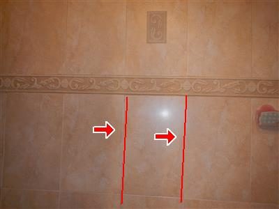 Beige ceramic tile shower wall with two vertical grout lines traced in red and two red arrows.