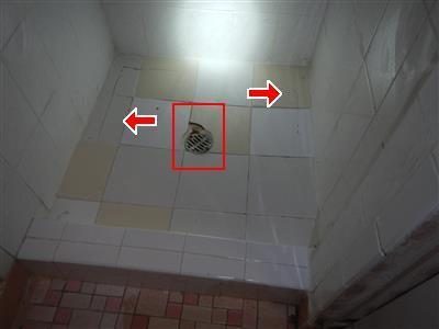 White tiled shower floor with a drain cover outlined in a red box and two red arrows on cracked tiles.