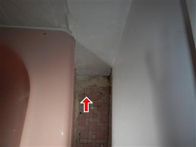 Corner beside a pink bathtub where small pink tiles are smeared with grout, marked by a red arrow.