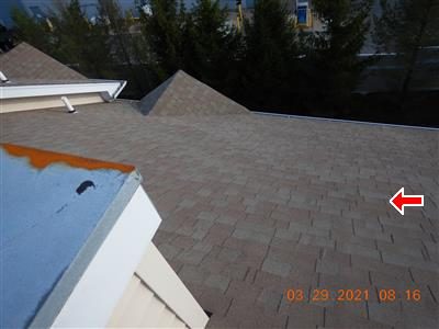 View across a brown asphalt shingle roof toward the rear, with a red arrow on the shingle field.