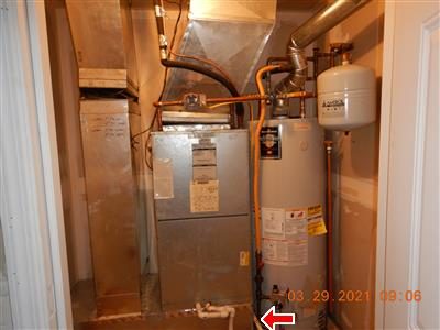 Utility closet with a furnace air handler, gas water heater and expansion tank, with a red arrow at the floor beneath the unit.