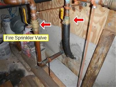 Copper supply piping in a basement with two valves marked by red arrows and a label reading Fire Sprinkler Valve.