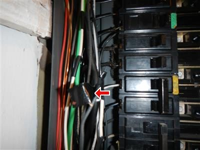 Inside an electrical panel with bundled wires; a red arrow points at a black-taped wire joint on the left side beside the breakers.
