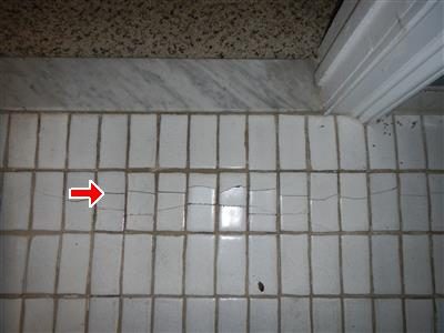 Small white floor tiles with a horizontal crack running across several tiles, marked by a red arrow.
